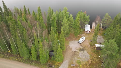 sweden - lakeside forest with vibrant autumn colors, dirt road, and white campervan on a cloudy day - aerial panning