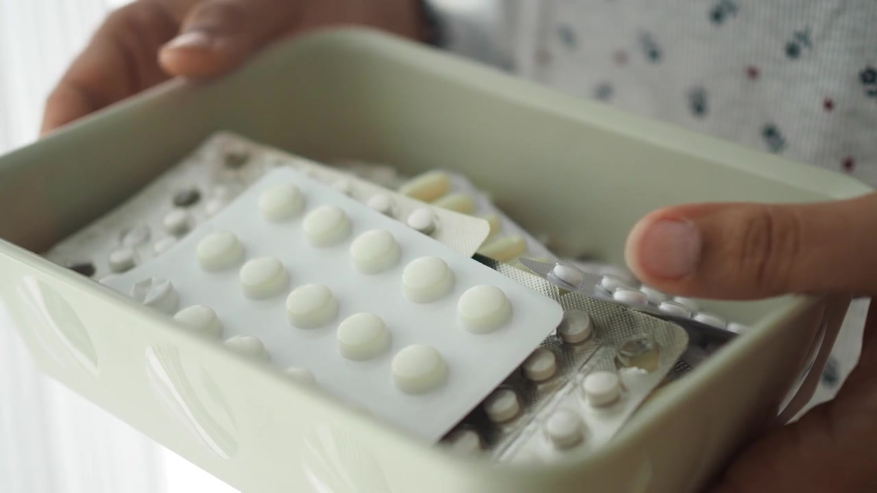 Person Holding a Container Filled with Various Medication Blister Packs