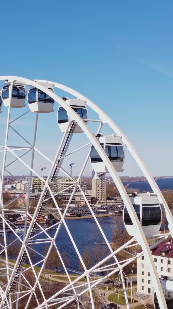 Ferris wheel slowly turning, with city scape of Riga under a clear blue sky