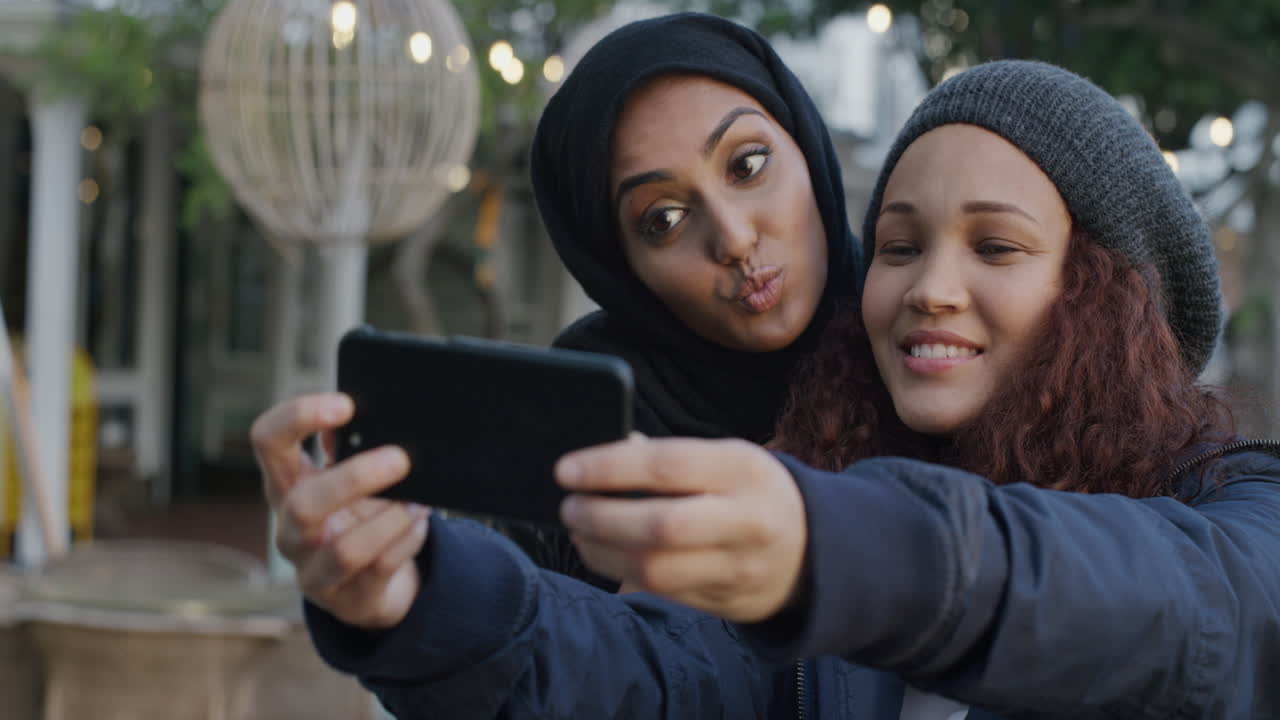 retrato de jóvenes mujeres multiétnicas amigas usando teléfonos inteligentes tomando selfies tomando fotos haciendo caras disfrutando de una diversión relajada amigas felices pasando el rato en la ciudad juntas en cámara lenta