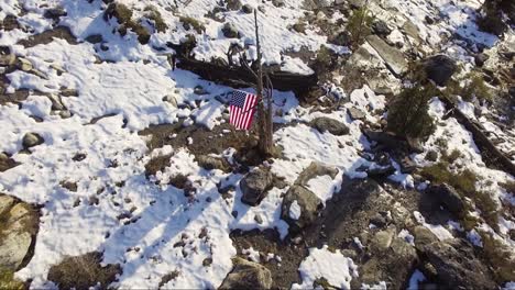 aerial drone orbit shot of an american flag hanging on a snowy, rocky mountain top