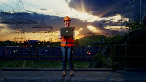 cuerpo lleno de ingeniera femenina asiática con casco de seguridad trabajando en una computadora portátil mientras estaba de pie cerca de la torre de alto voltaje