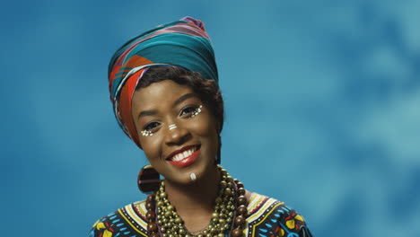 vista de cerca de una joven afroamericana alegre con turbante y maquillaje sonriendo alegremente a la cámara