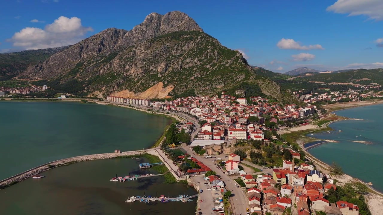 Eğirdir Gölü yarımadasındaki yoğun kırmızı çatılı konutların üzerinden alçak açılı havadan uçuş. Türkiye'de geleneksel göl kenarı kasaba mimarisi ve kıyı topluluğu.