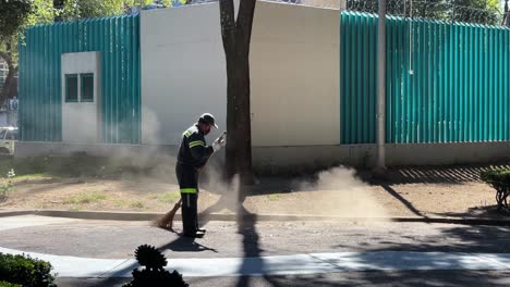 un hombre en mexico usa una escoba para barrer el suelo afuera en un parque