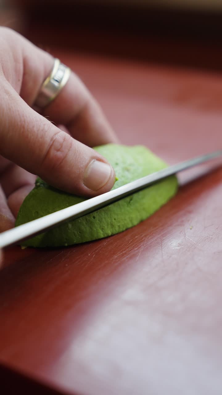 Knife cut long green avocado slices on wooden board, vertical close up view
