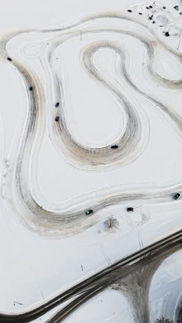 vertical drone shot overlooking cars driving on a rural ice track, winter day