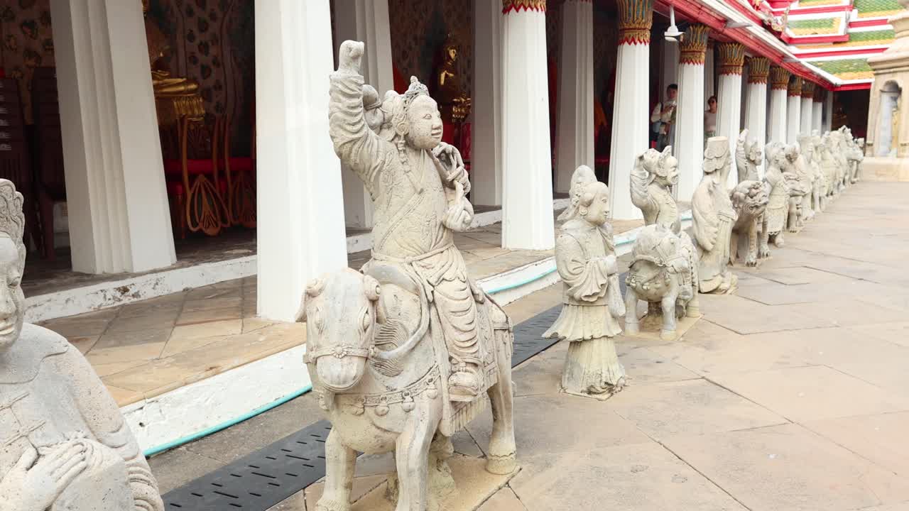 Stone statues line the walkway of Wat Arun Temple, Bangkok. Bright daylight illuminates intricate carvings and temple architecture