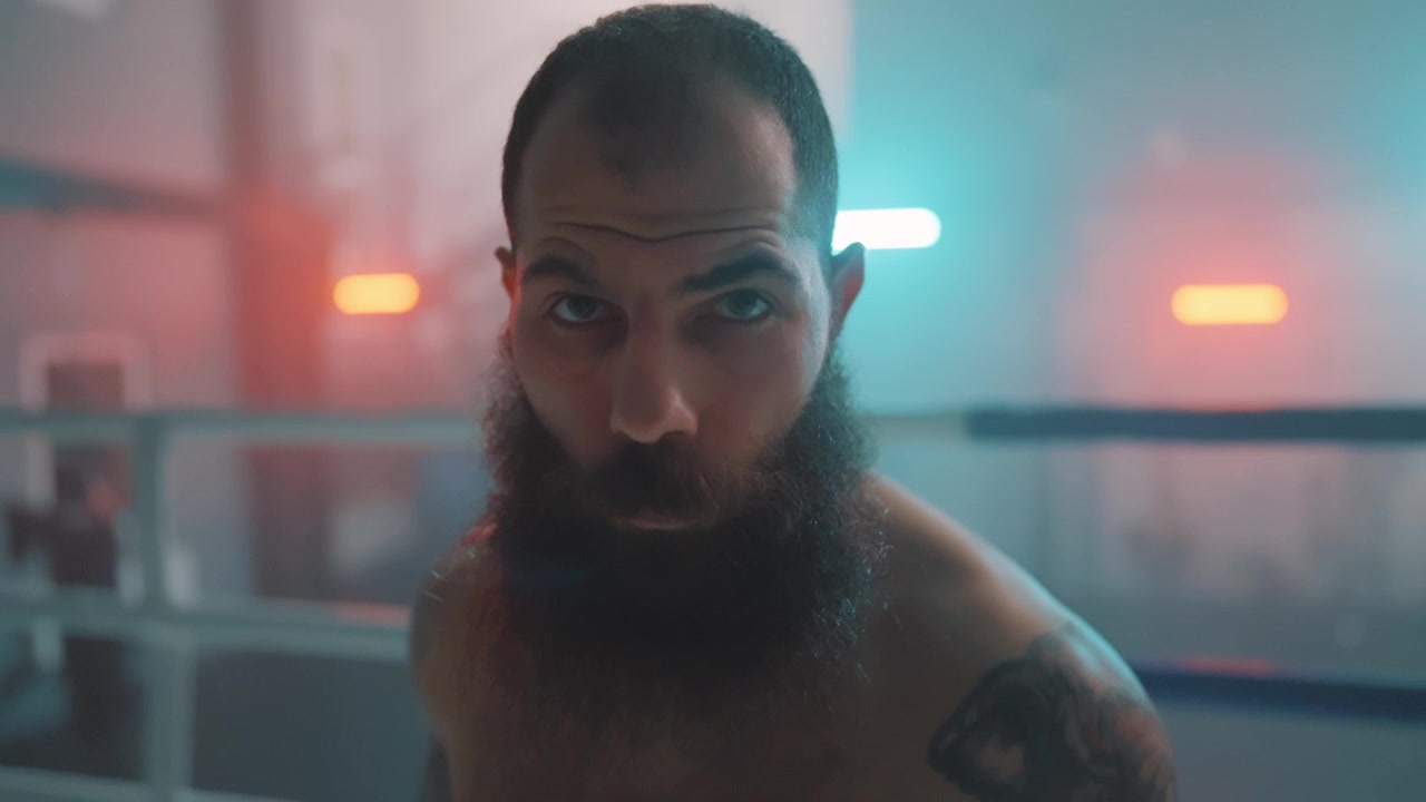 Boxeador Barbudo Intenso Olhando Fixamente para a Câmera em um Ringue de Boxe Esfumaçado