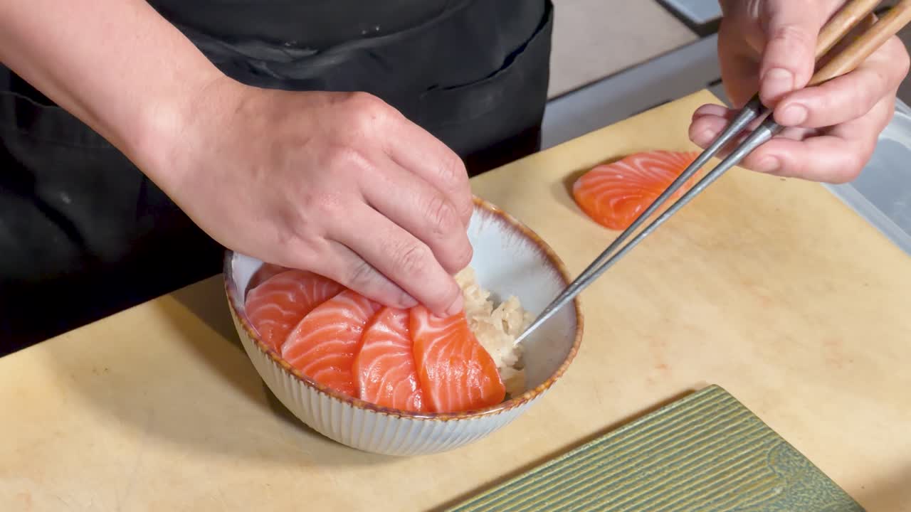 Vista dall'alto di uno chef che sistema con cura le fette di sashimi di salmone sulla ciotola di riso sotto una luce intensa