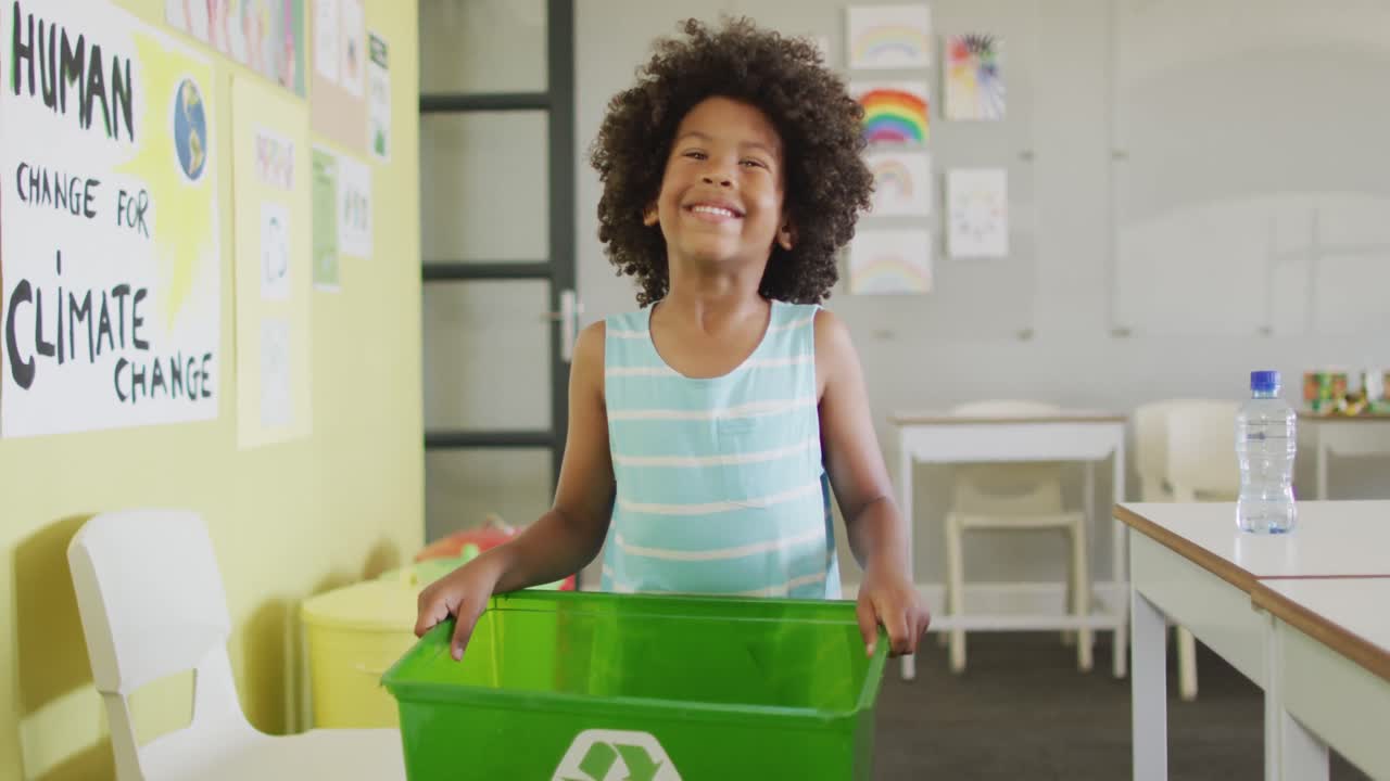 video de un niño afroamericano feliz sosteniendo una caja con un símbolo de reciclaje en el aula