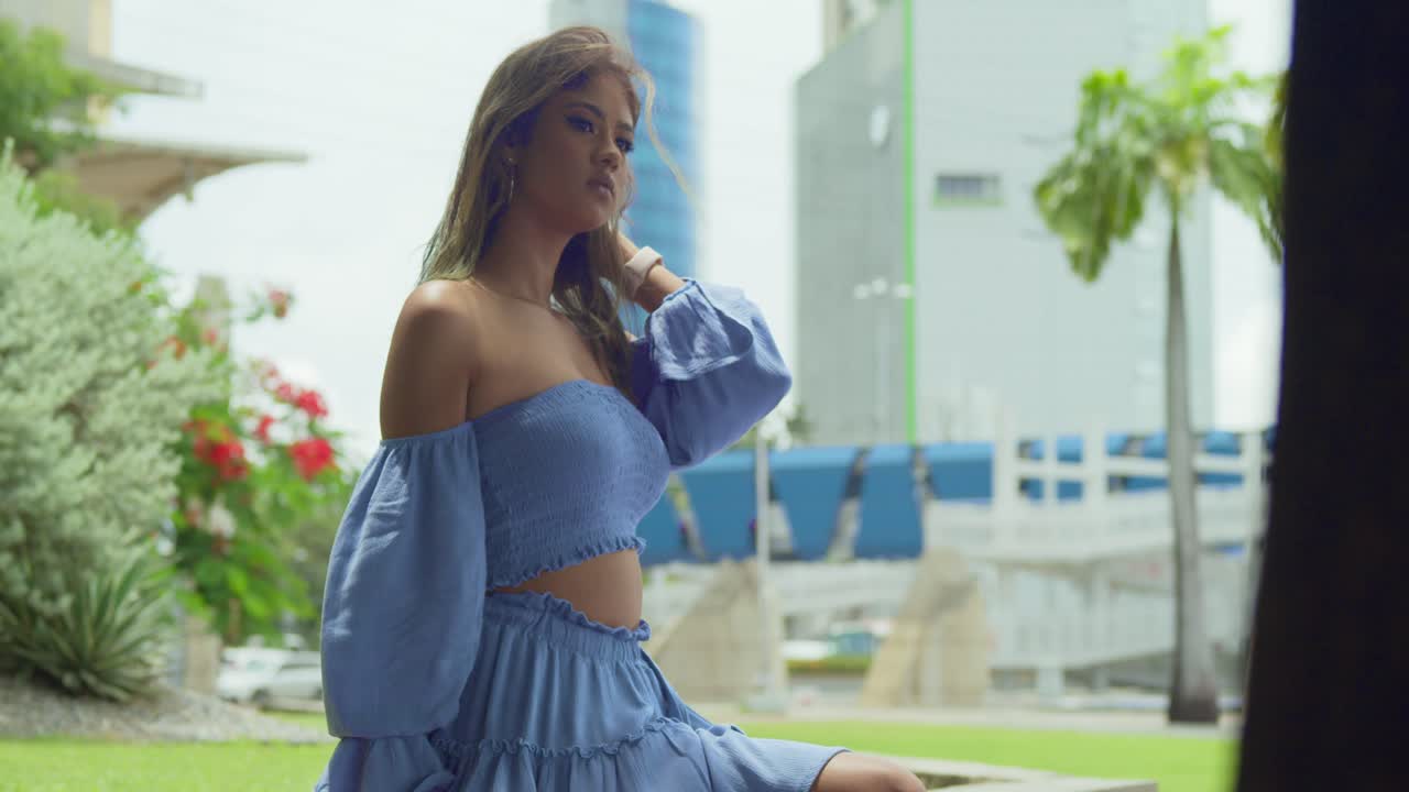 pan a la derecha con un vestido azul de niña que sopla en el viento mientras está sentado en la ciudad de puerto españa, trinidad