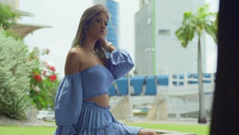 pan right with a girl blue dress blowing in the wind while sitting in the city of port of spain, trinidad