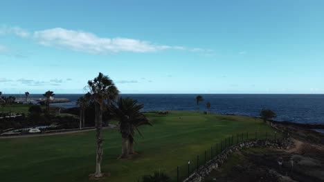 Dolly-Aéreo-Delante-Del-Campo-De-Golf-Con-Vistas-Al-Agua-Azul-Del-Océano-En-La-Costa-De-España