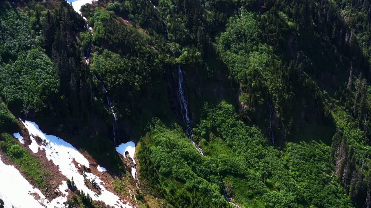 Scenic aerial shot descending and slowly zooming in on small waterfall on the cliff side surrounded by lush greenery in the Pacific Northwest, Washington State.