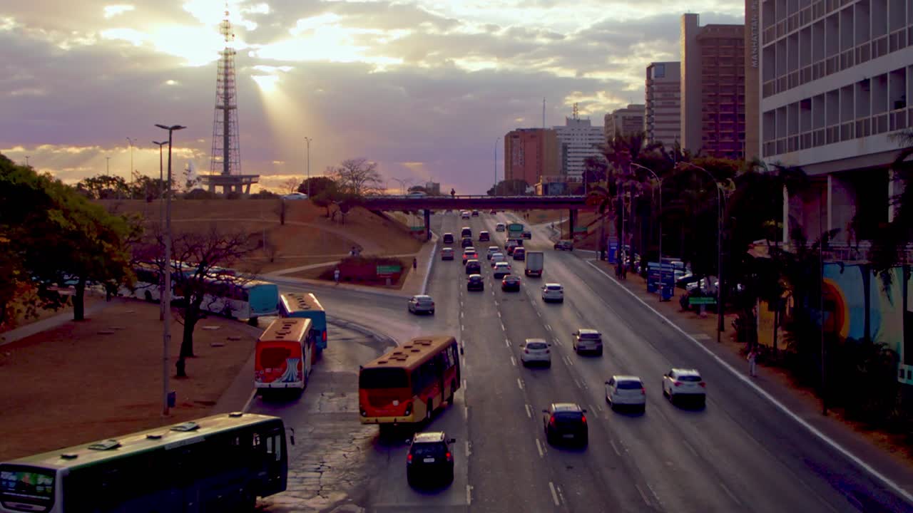 Timelapse del tráfico en autopista urbana al atardecer con nubes y rayos de sol sobre una torre de transmisión de televisión - timelapse de nubes