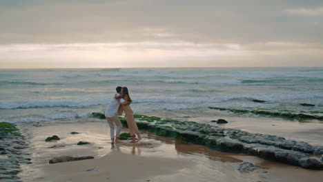 Married-newlyweds-having-fun-at-wavy-coastline.-Man-carrying-woman-vertical-view