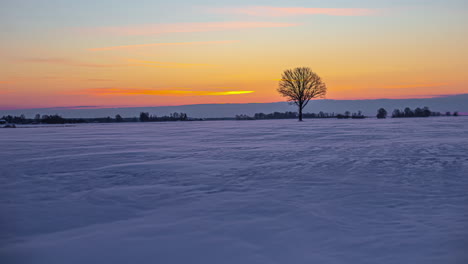lapso de tiempo de nubes moviéndose sobre un cielo de color puesta de sol mientras la nieve sopla sobre un campo