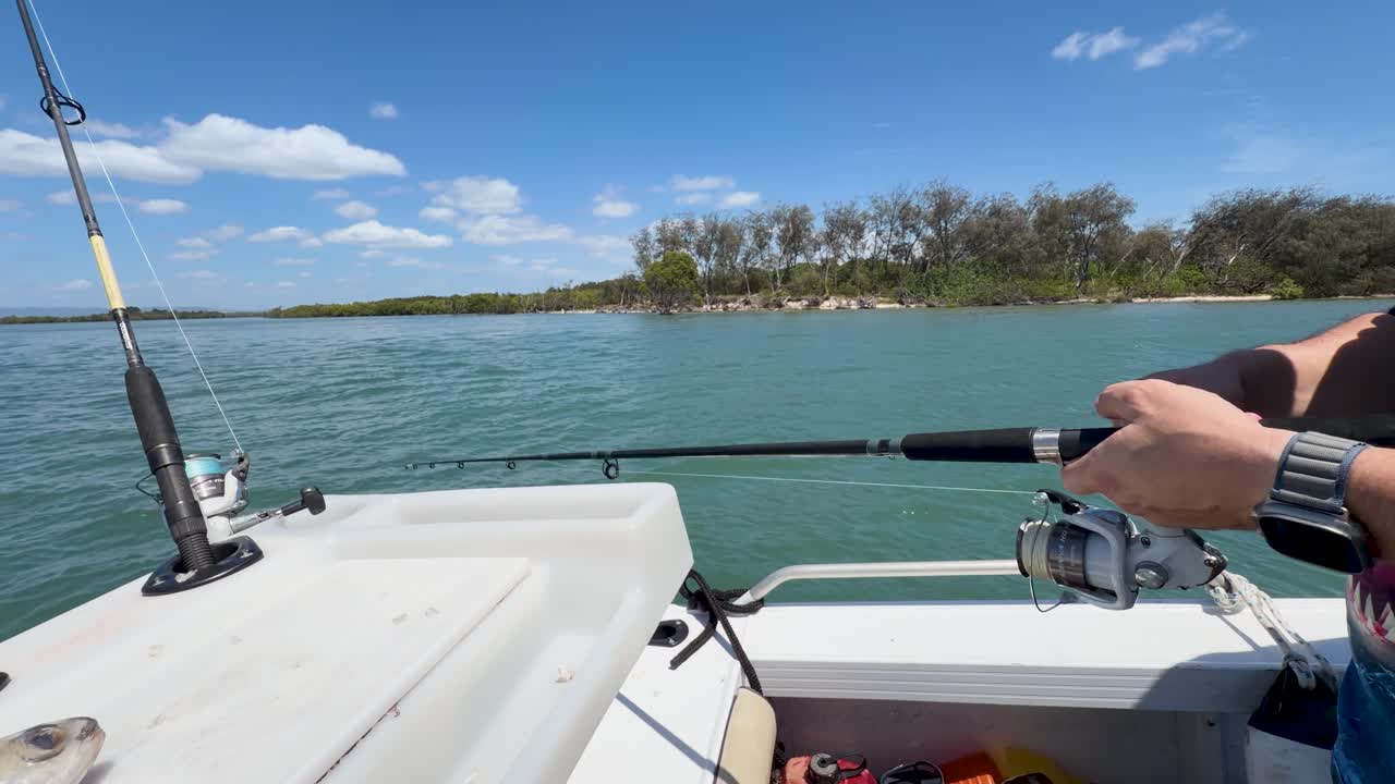 Un pescatore tiene in mano una canna da pesca mentre si trova su una barca al largo durante una giornata di sole