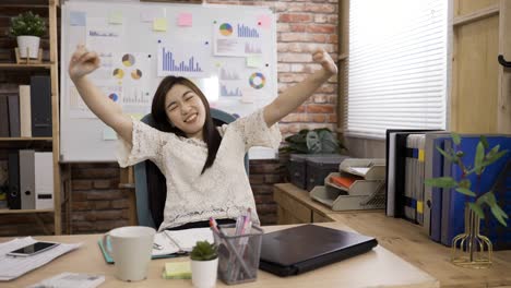 asian female creative worker closing her laptop is exercising her neck muscles and stretching her body feeling happy about getting work done in the office.