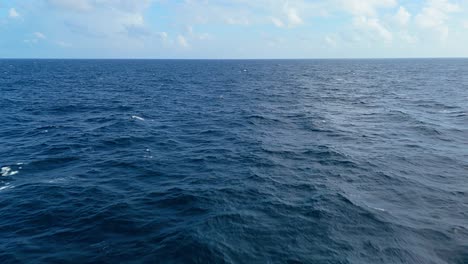 slow aerial push in above soothing caribbean blue deep ocean sea water with clouds on horizon