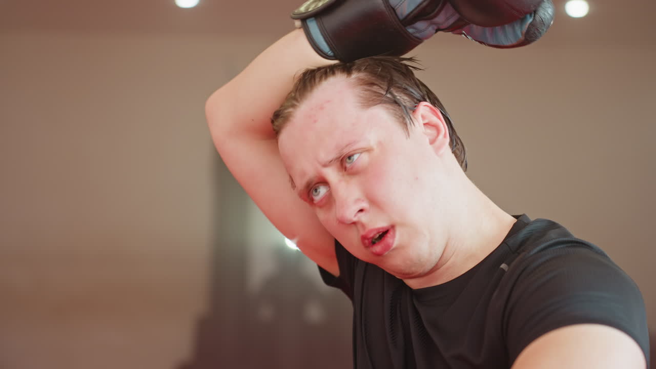 Male fighter exhausted after intense sparring session in gym, sweating heavily with wet hair falling over face, wearing black sportswear, head down showing fatigue, physical strain under training lights