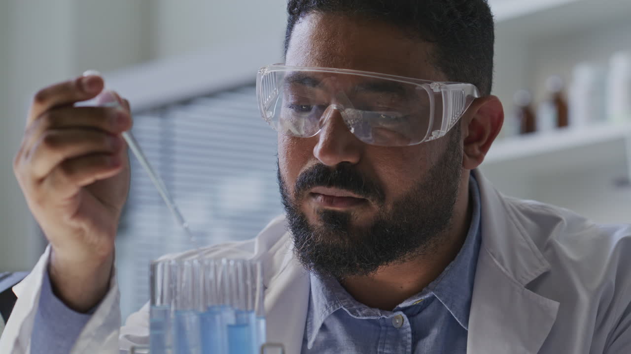 Chemist in Safety Goggles Transferring Blue Liquid into Test Tubes