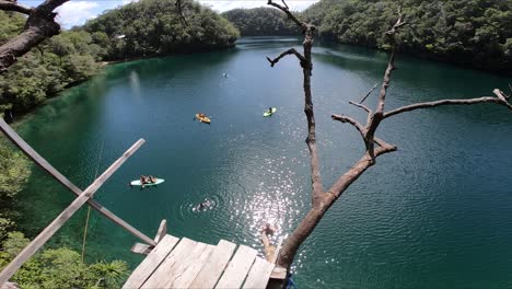 A-young-white-man-with-blonde-long-hair-is-jumping-from-a-wooden-platform,-high-up-on-a-hill,-into-the-crystal-clear-water-in-Siargao,-Philippines