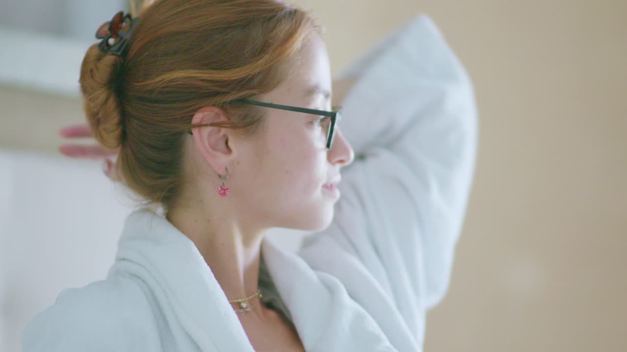Young woman in robe touching hair in room