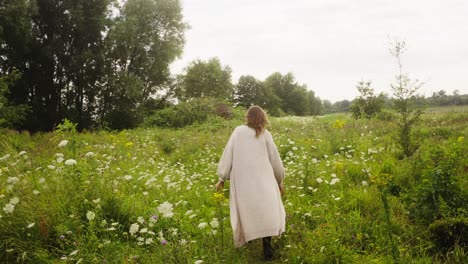 a-woman-in-a-robe-enters-a-garden-of-white-flowers-in-bloom,-girl-was-walking-in-the-park-in-the-afternoon-with-the-soft-sunlight-use-her-hands-to-gently-touch-the-white-flowers,-4k