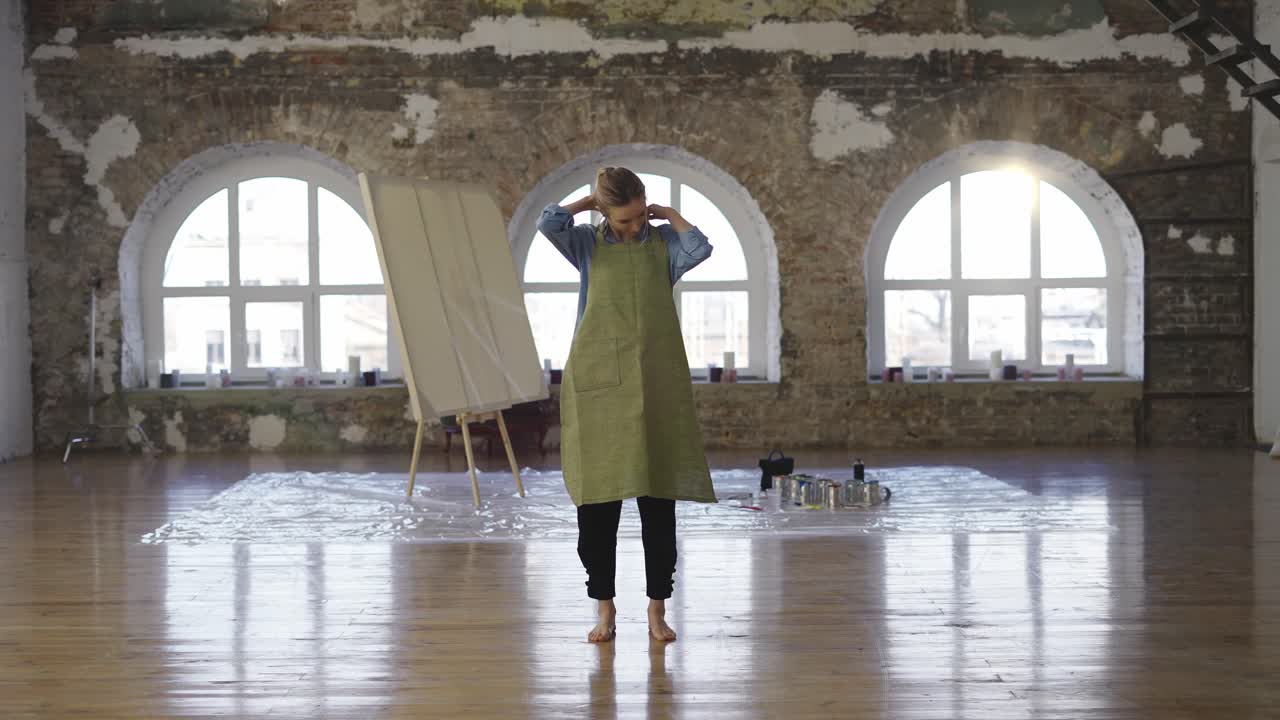 Full length woman put on apron to start painting in large workshop