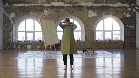 full length woman put on apron to start painting in large workshop