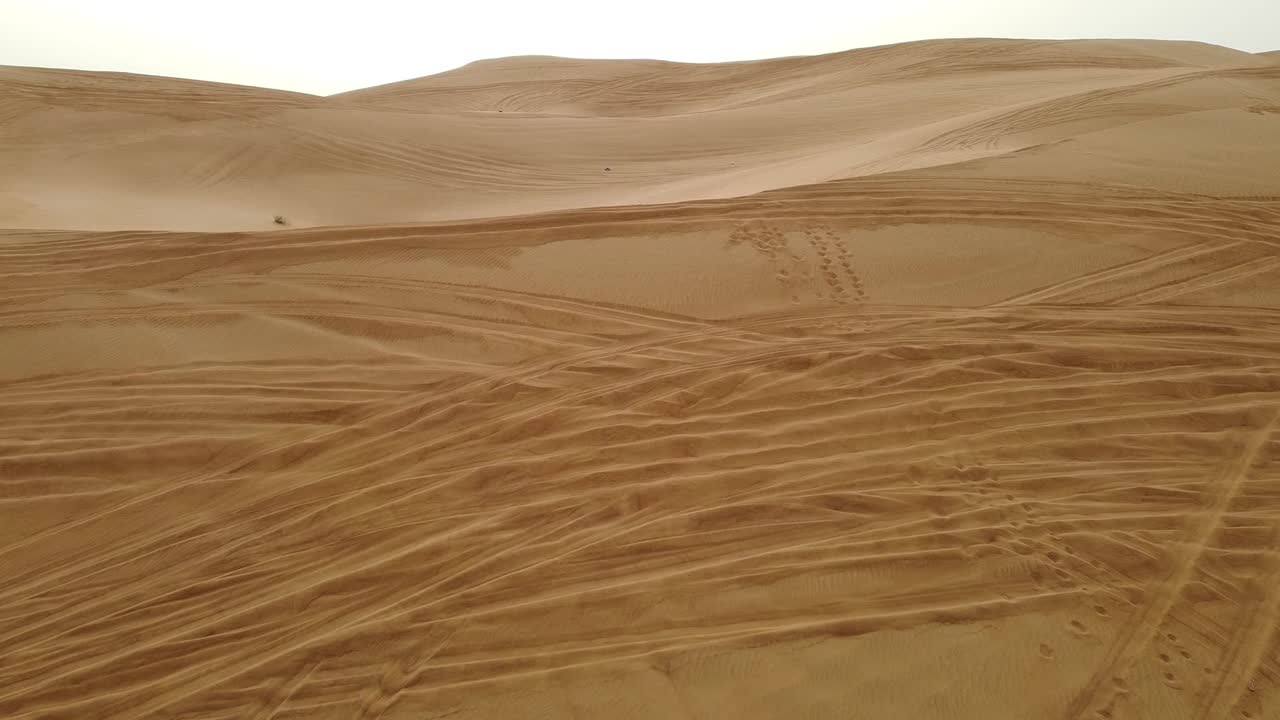 drone filmado volando sobre el desierto de dubai con vehículos y huellas humanas en la arena