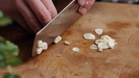 Männlicher-Koch,-Der-Knoblauch-In-Dünne-Scheiben-In-Der-Küche-Auf-Einem-Holzschneidebrett-In-Der-Küche-Schneidet