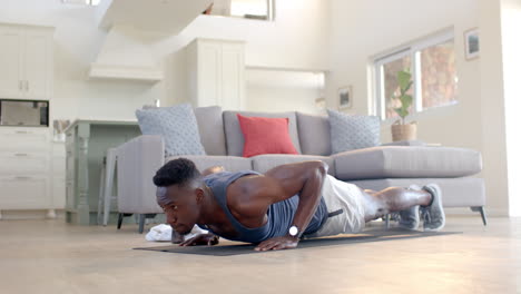 un hombre afroamericano concentrado haciendo flexiones en una sala de estar soleada, en cámara lenta.