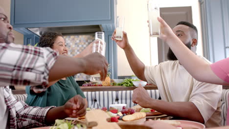 diverse friends toasting with glasses of milk while enjoying meal together at home