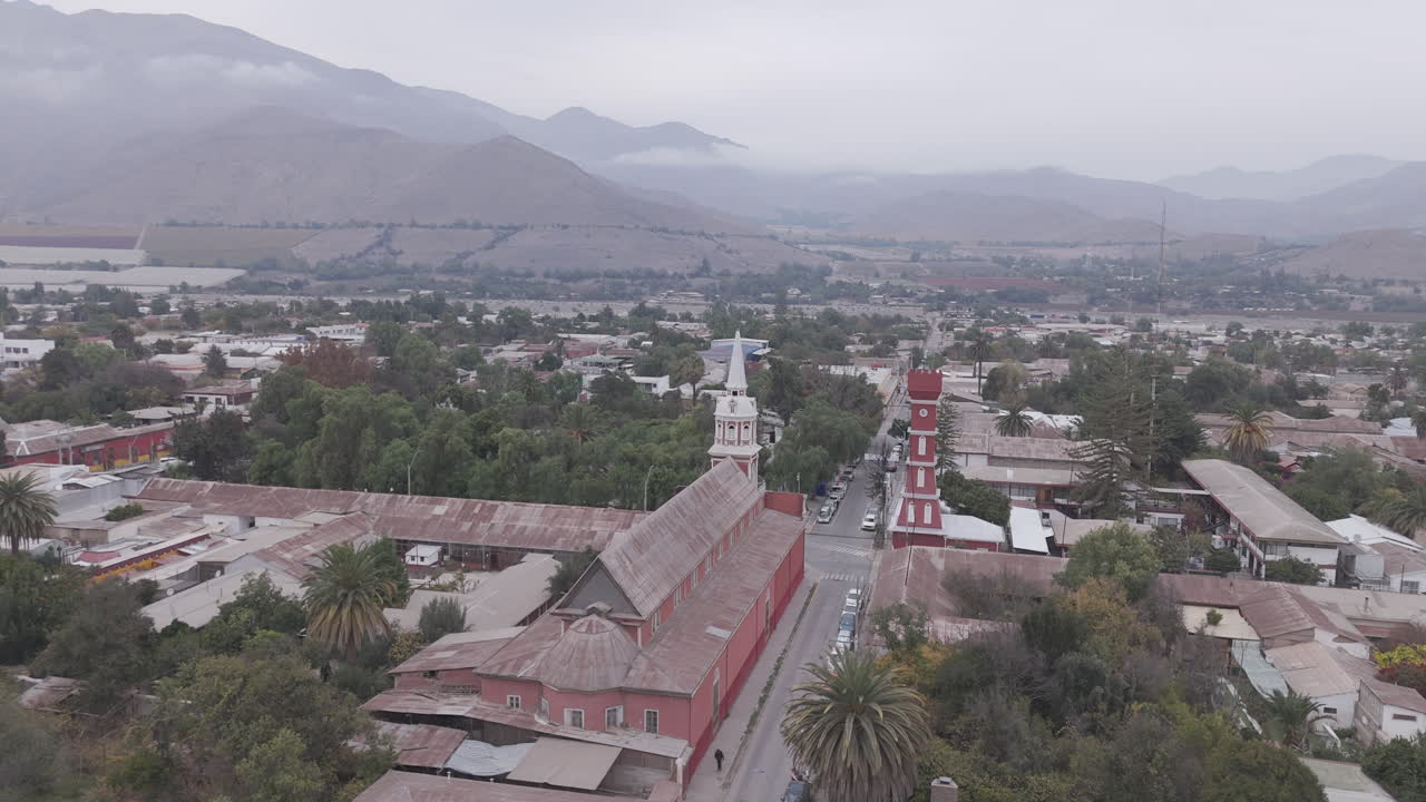 Spiral drone shot around the town of Vicuña near Coquimbo in Chile South America with the main square and red tower Torre Bauer visible on a grey day with mountains in the background LOG