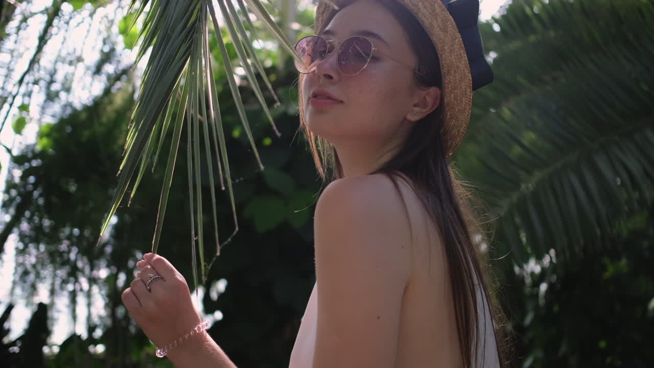 Donna con cappello di paglia e occhiali da sole in un giardino tropicale
