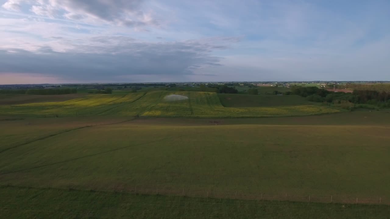 rociador de agua grande en el campo de colza en la noche de verano en el sur de suecia skåne österlen kåseberga, antena lenta hacia adelante