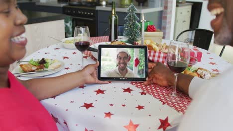 Pareja-Afroamericana-Sonriente-Usando-Una-Tableta-Para-Una-Videollamada-Navideña-Con-Un-Hombre-En-La-Pantalla