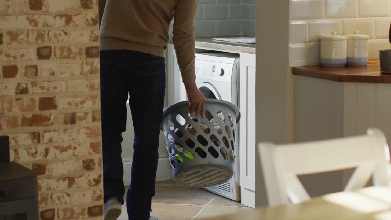 Happy caucasian man holding basket and doing laundry in kitchen