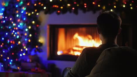 A-Young-Man-Admires-The-Fire-In-The-Fireplace-Which-Is-Decorated-With-Garlands-For-Christmas