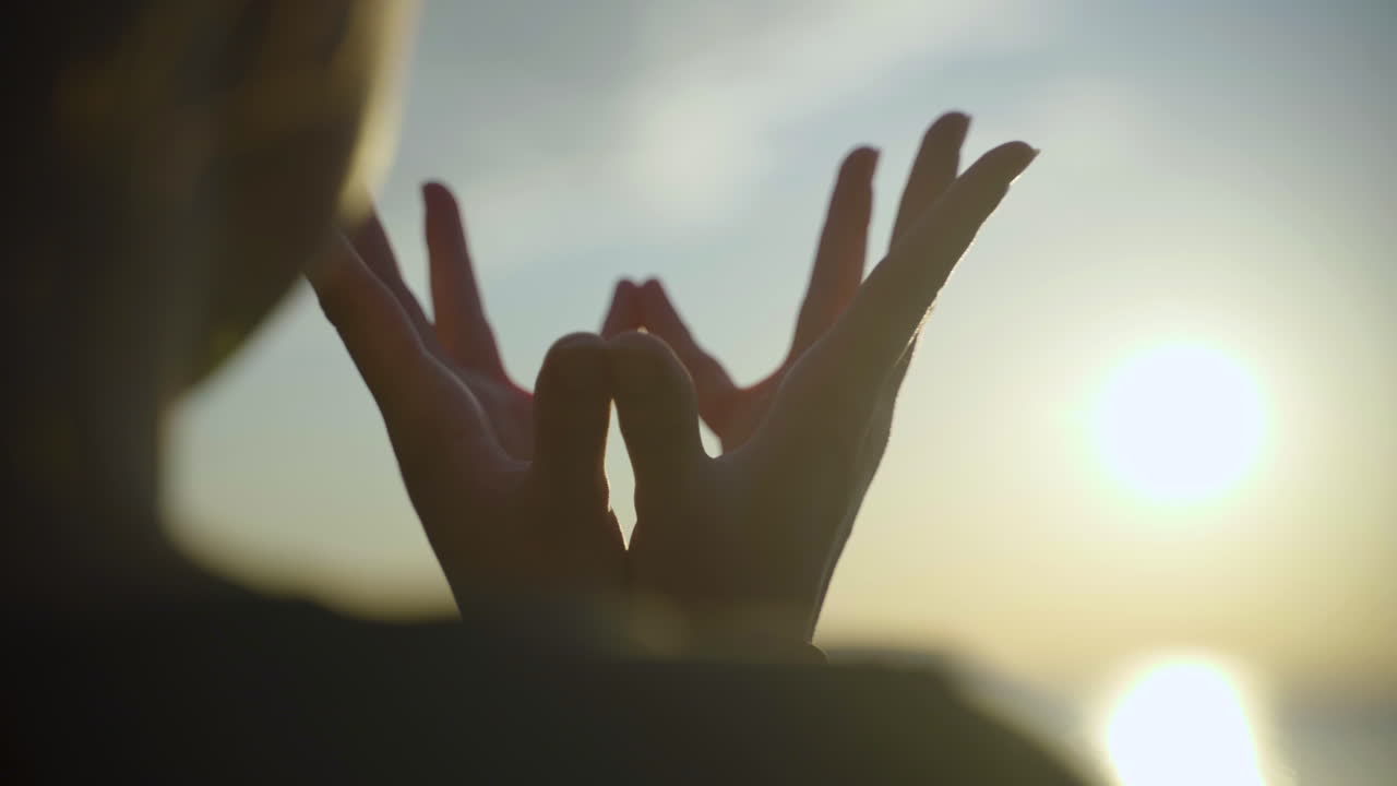 Silhouette of woman's hands in Padma Mudra beside the lake at sunrise.