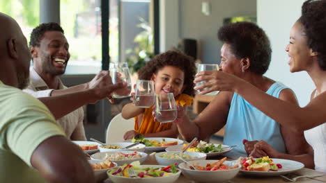 Familia-Multigeneracional-Alrededor-De-La-Mesa-Haciendo-Aplausos-Con-Agua-Antes-De-Servir-Comida-En-Casa