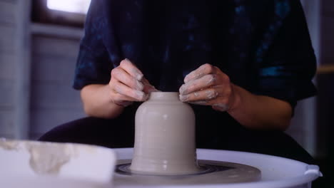 Potter-puts-finishing-touches-on-clay-vase-on-pottery-wheel-in-her-workshop-closeup-on-clay-vase