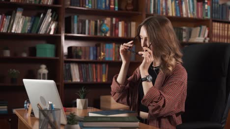 la niña se limpia las gafas, se las pone, toma un libro en sus manos, y comienza a leer mientras trabaja simultáneamente en su portátil