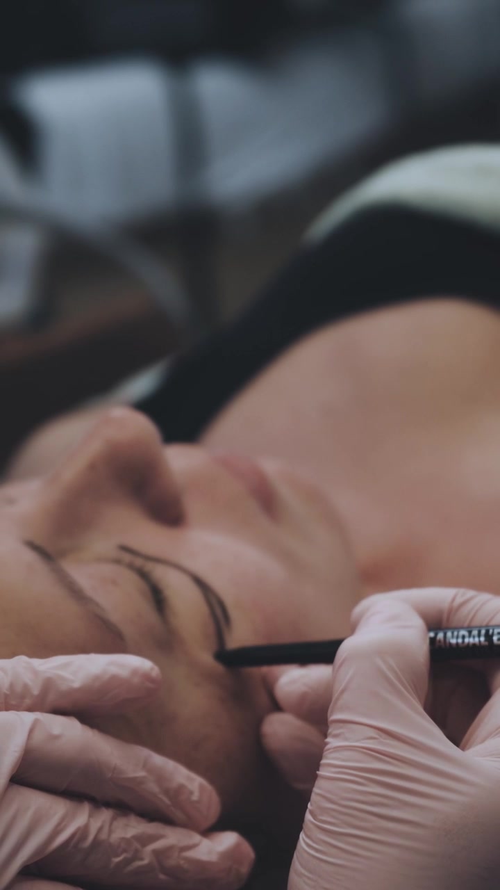 Kosmetikerin zeichnet Augenbrauenform bei einer Kundin vor einer Microblading-Behandlung.