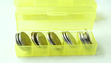 close up of coins in a plastic box on yellow background