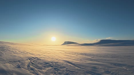 Snow drifts across Nordic winter landscape, low evening sun on horizon