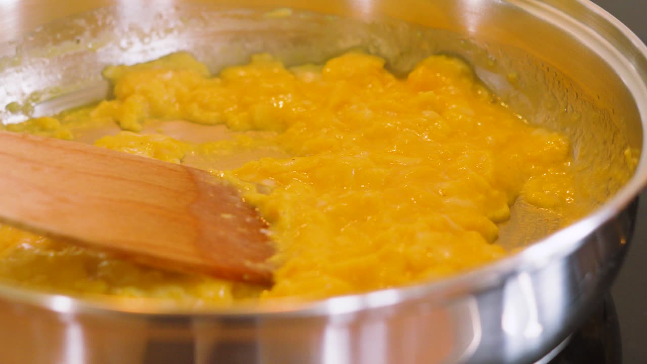 Side View of Scrambled Eggs Being Cooked in Frying Pan with Wooden Spatula to Make Healthy Morning Breakfast Meal. Cooking Food Photography.
